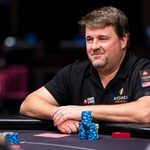 Chris Moneymaker seated at a poker table, wearing a black PokerStars Team Pro shirt with stacks of blue poker chips in front of him.