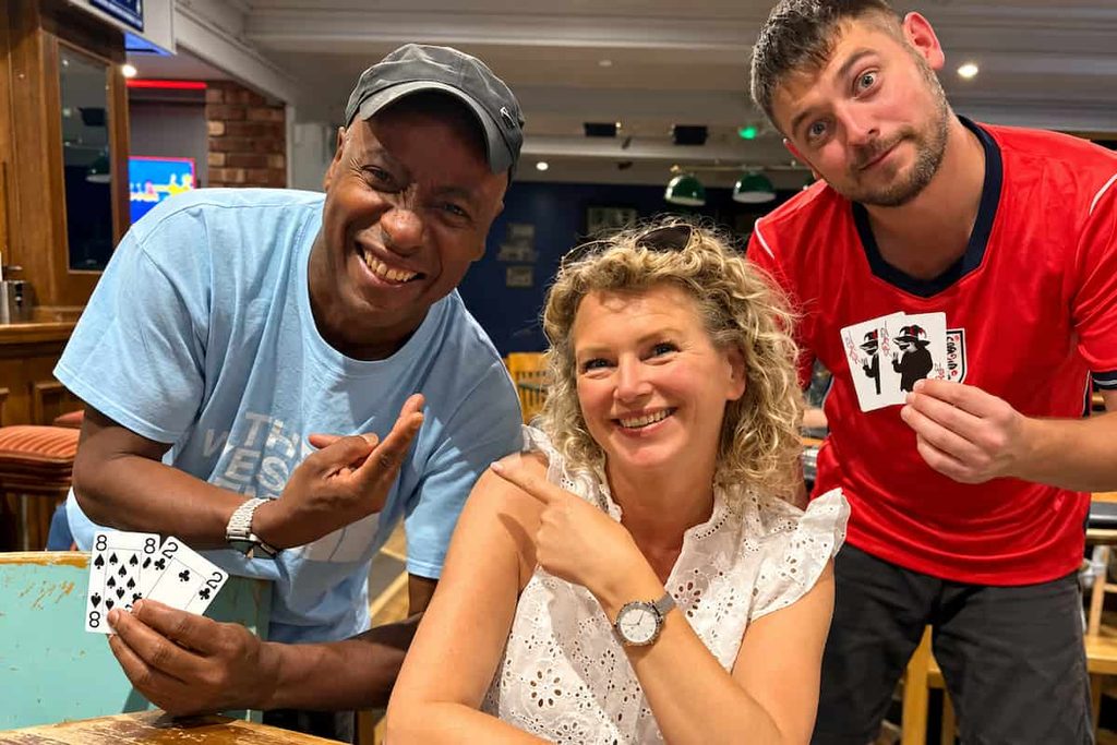 Nuneaton teacher Nicki Kelsall smiles alongside two fellow poker players at a local poker league event, where players show off their cards.